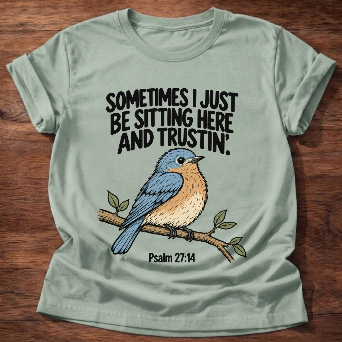 Sage t-shirt printed with a bluebird on a branch graphic and 'Sometimes I just be sitting here and trustin'.' Psalm 27:14 faith based gift