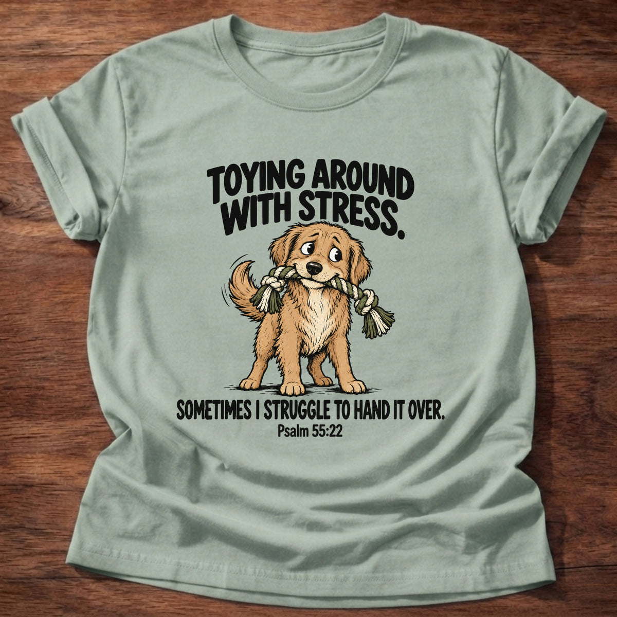 Sage t-shirt printed with a dog tugging a rope toy graphic and 'Toying around with stress. Sometimes I struggle to hand it over.' Psalm 55:22 faith based gift