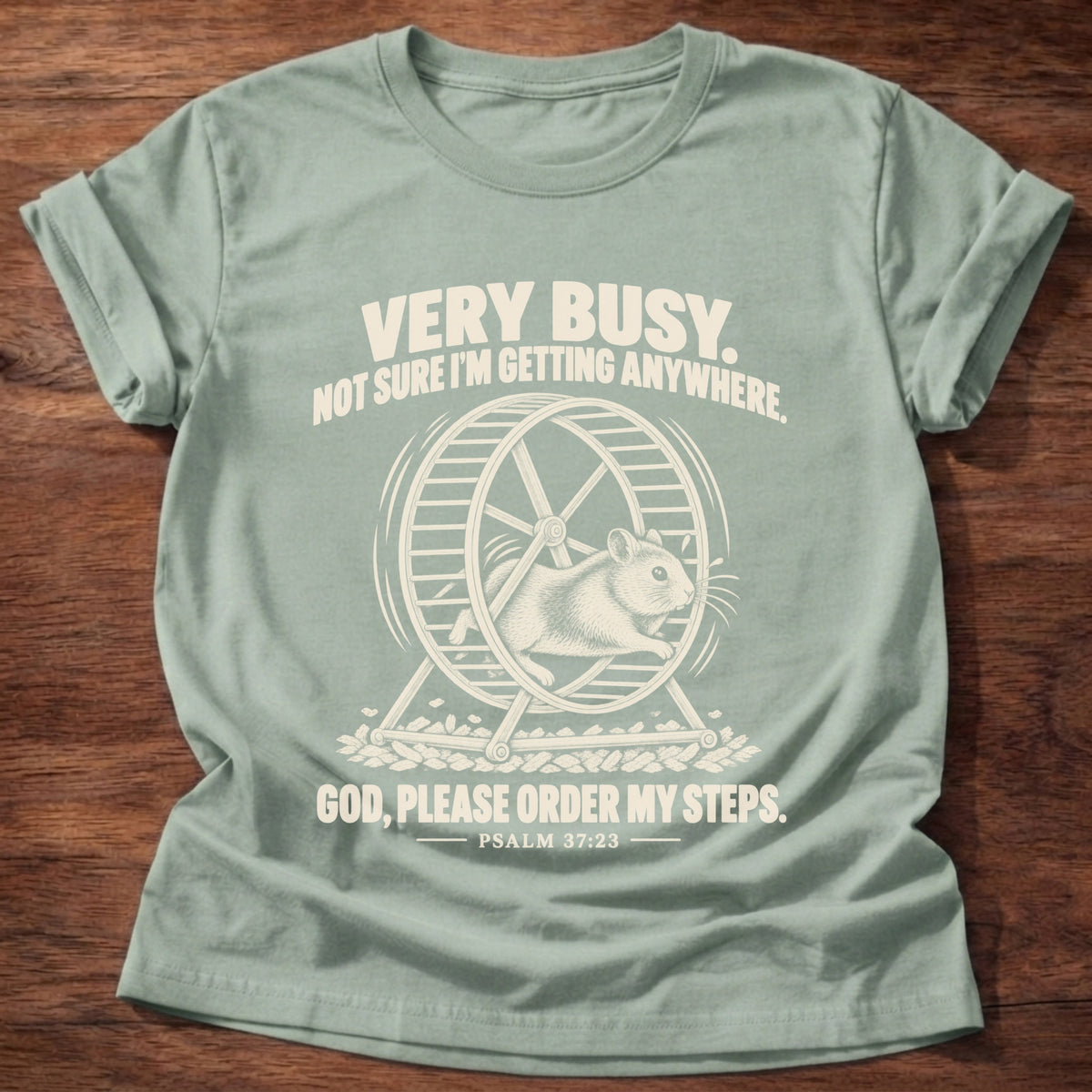 Sage t-shirt printed with a squirrel running on a wheel graphic and 'Very busy. Not sure I'm getting anywhere. God, please order my steps.' Psalm 37:23 faith based gift