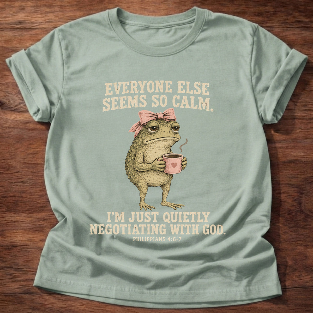 Sage t-shirt printed with a possum holding a tea cup graphic and 'Everyone else seems so calm. I'm just quietly negotiating with God.' Philippians 4:6-7 faith based gift