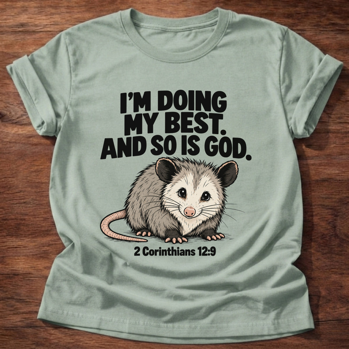 Sage t-shirt printed with an opossum graphic and 'I'm doing my best. And so is God.' 2 Corinthians 12:9 faith based gift