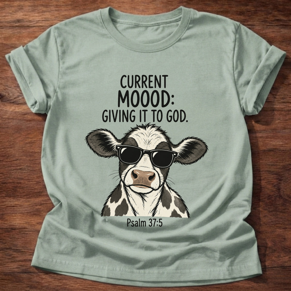 Sage t-shirt printed with a sunglasses-wearing cow graphic and 'Current moood: giving it to God.' Psalm 55:22 faith based gift