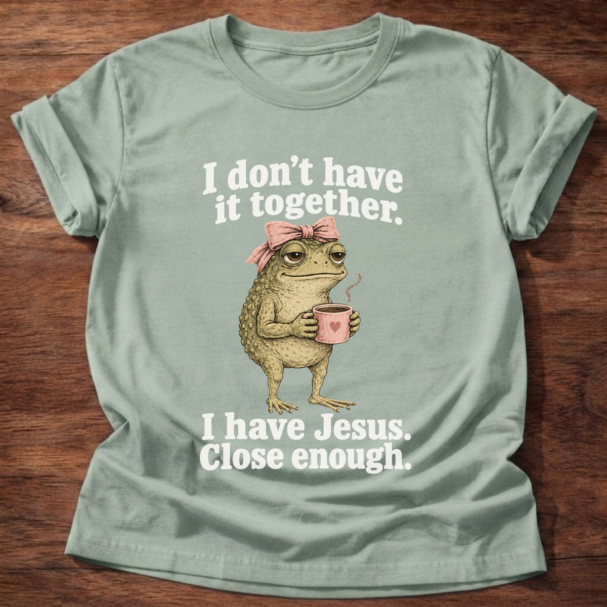 Sage t-shirt printed with a frog holding a tea cup graphic and 'I don't have it together. I have Jesus. Close enough.' 2 Corinthians 12:9 faith based gift