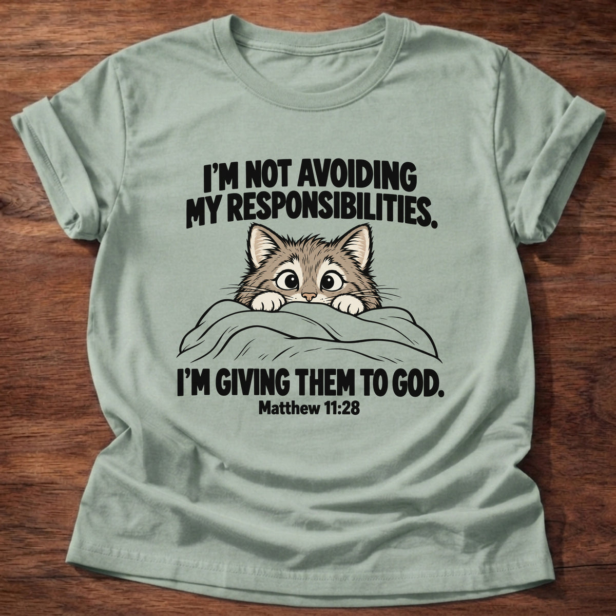 Sage t-shirt printed with a cat peeking over a blanket graphic and 'I'm not avoiding my responsibilities. I'm giving them to God.' Matthew 11:28 faith based gift