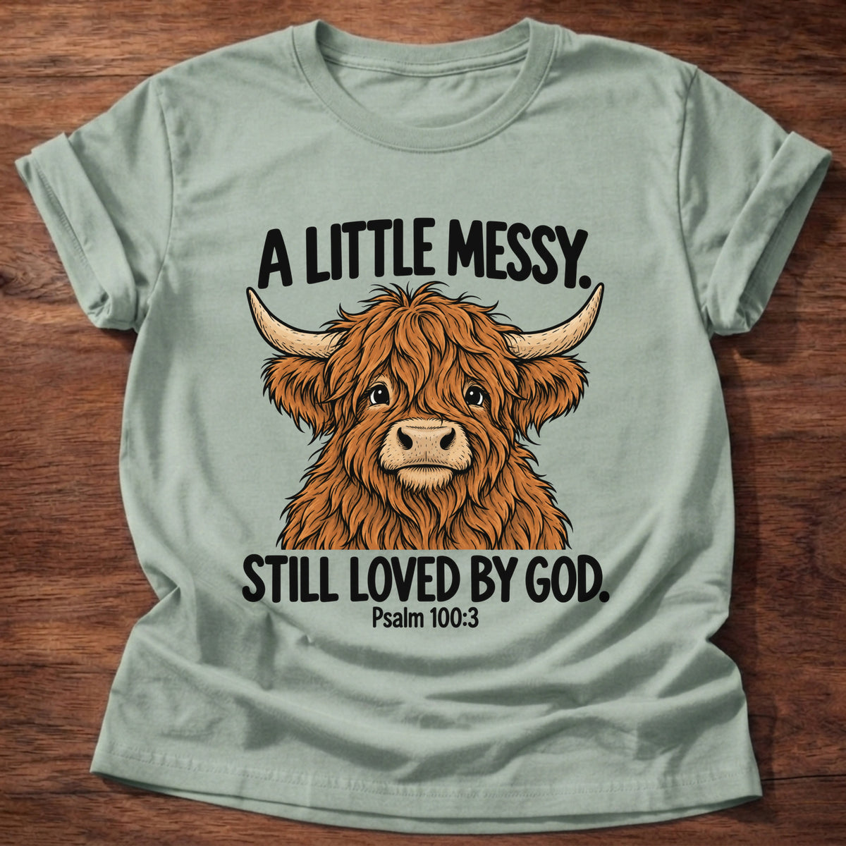 Sage t-shirt printed with a highland cow graphic and 'A little messy. Still loved by God.' Psalm 100:3 faith based gift