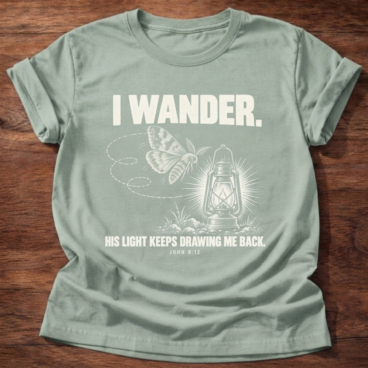 Sage t-shirt printed with a moth circling a glowing lantern graphic and 'I wander. His light keeps drawing me back.' John 8:12 faith based gift