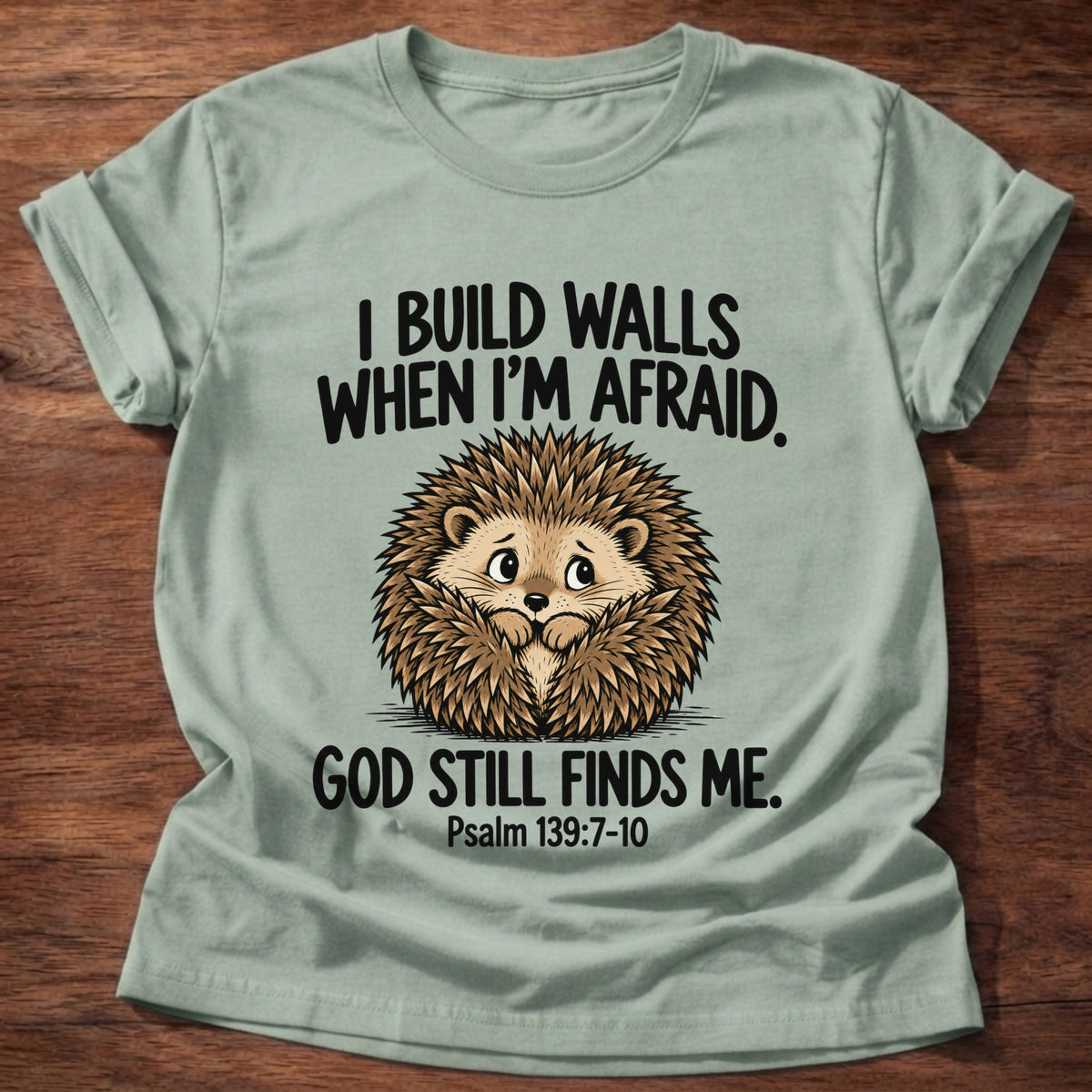 Sage t-shirt printed with a hedgehog curled into a ball and 'I build walls when I'm afraid. God still finds me.' Psalm 139:7-10 faith based gift