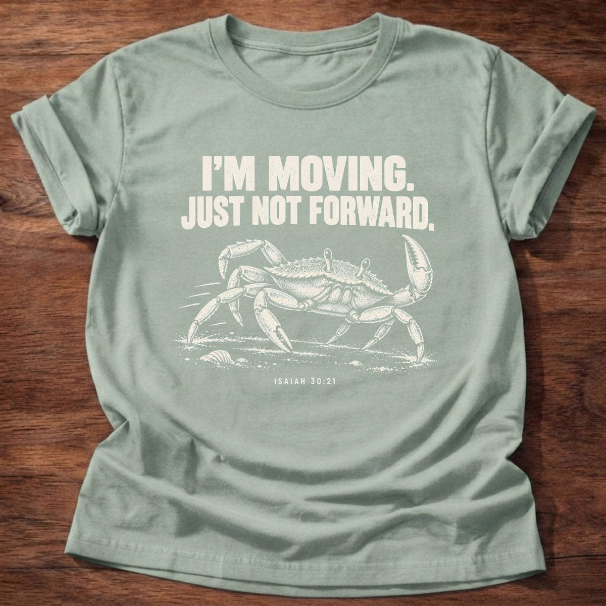 Sage t-shirt printed with a crab scuttling sideways across the sand graphic and 'I'm moving. Just not forward.' Isaiah 30:21 faith based gift