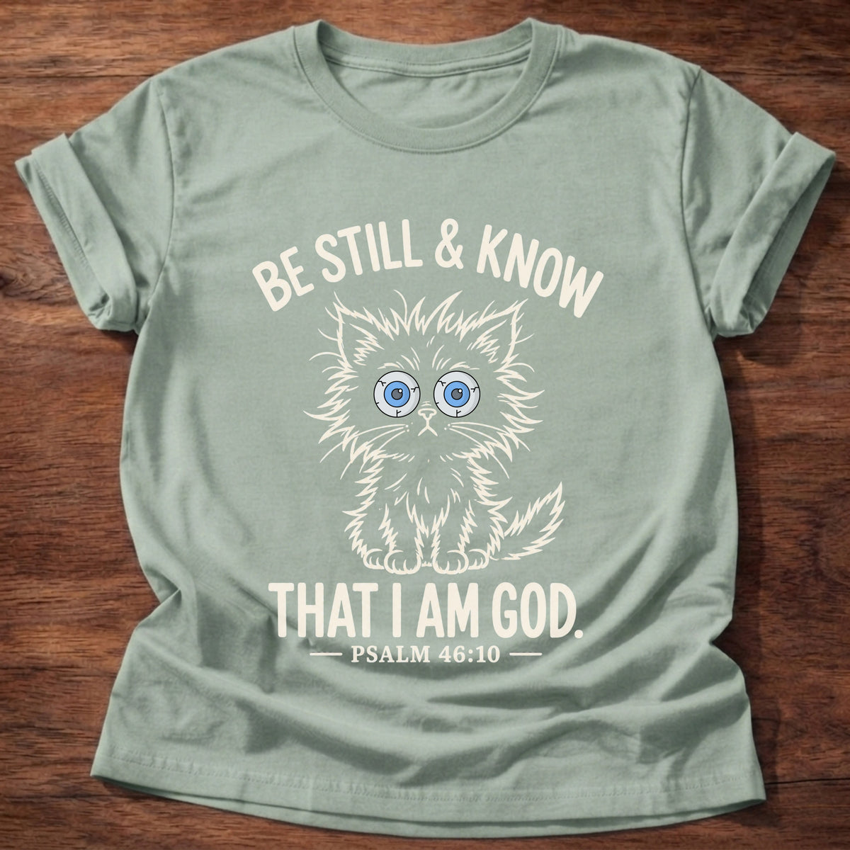 Sage t-shirt printed with a wide-eyed kitten sitting still graphic and 'Be still & know. That I am God.' Psalm 46:10 faith based gift