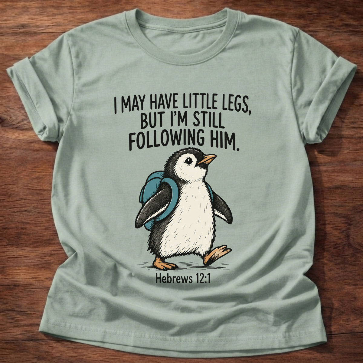 Sage t-shirt printed with a penguin graphic and 'I may have little legs, but I'm still following Him.' Hebrews 12:1 faith based gift