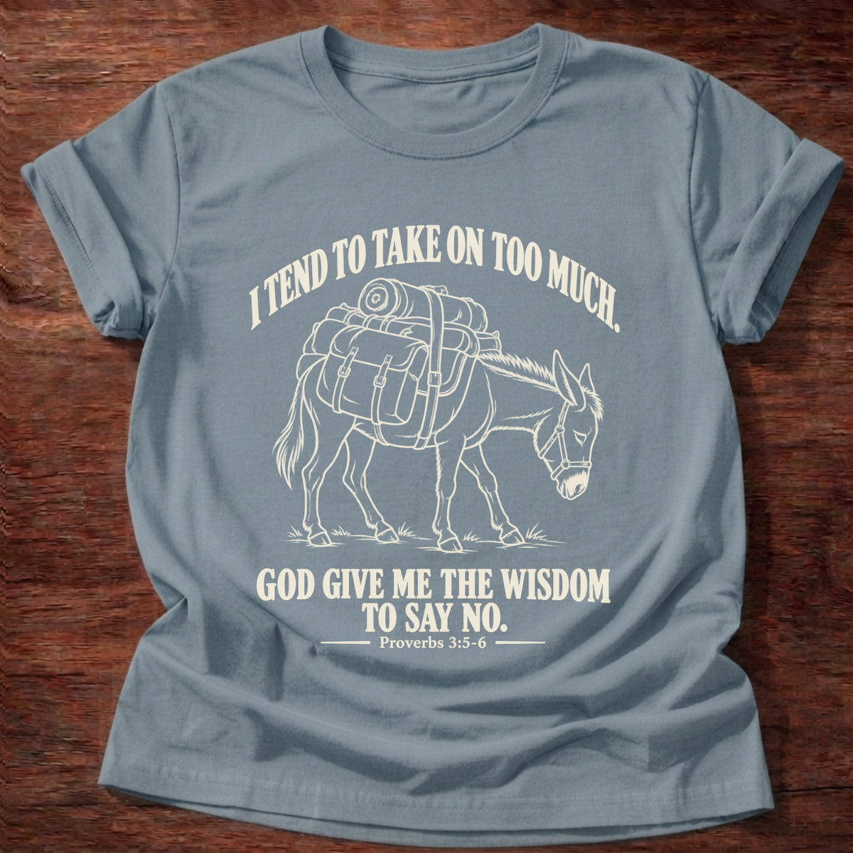 Stone Blue t-shirt printed with a pack donkey weighed down with overstuffed bags and bundles graphic and “I tend to take on too much. God give me the wisdom to say no.” Proverbs 3:5-6 faith based gift