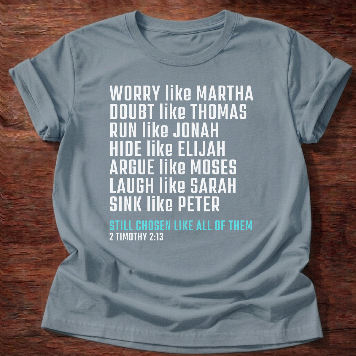 Stone Blue t-shirt printed with bold stacked typography listing Bible characters graphic and “Worry like Martha. Doubt like Thomas. Sink like Peter. Still chosen like all of them.” 2 Timothy 2:13 Christian shirt