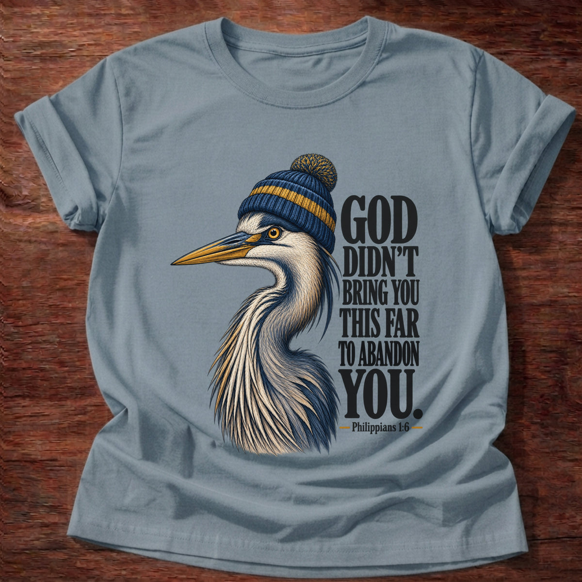 Stone Blue t-shirt printed with a great blue heron wearing a knit beanie graphic and “God didn't bring you this far to abandon you.” Philippians 1:6 faith based gift