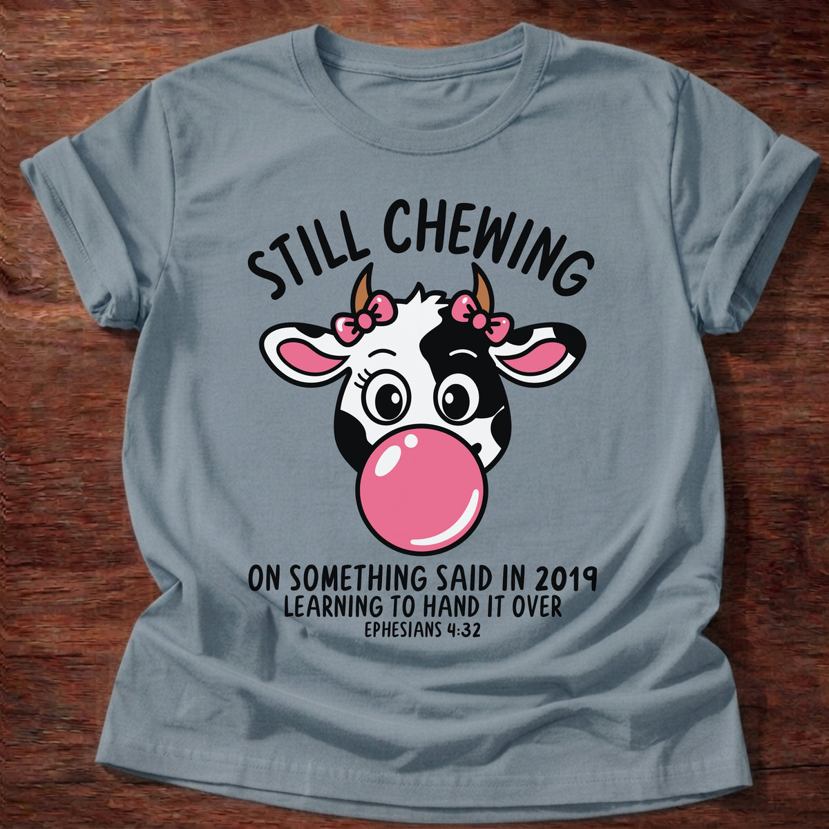 Stone Blue t-shirt printed with a cow blowing a bubblegum bubble and “Still chewing on something said in 2019. Learning to hand it over.” Ephesians 4:32 Christian shirt