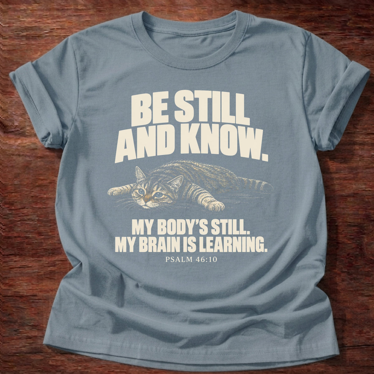Brain Is Learning T-Shirt in Stone Blue featuring a relaxed cat stretched out lying down and Psalm 46:10 overthinking humor design