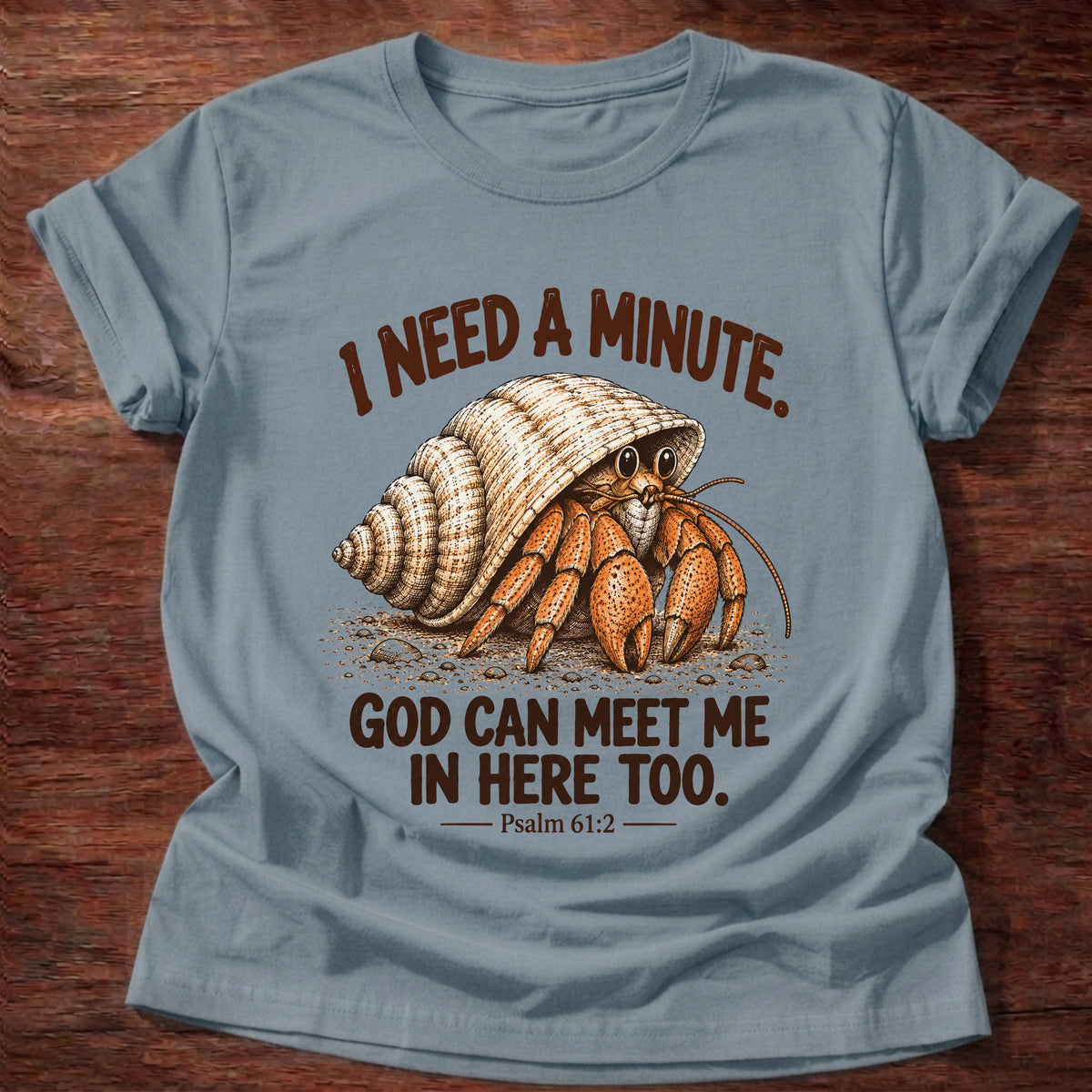 Stone Blue t-shirt printed with a hermit crab peeking out of its spiral shell graphic and “I need a minute. God can meet me in here too.” Psalm 61:2 faith based gift