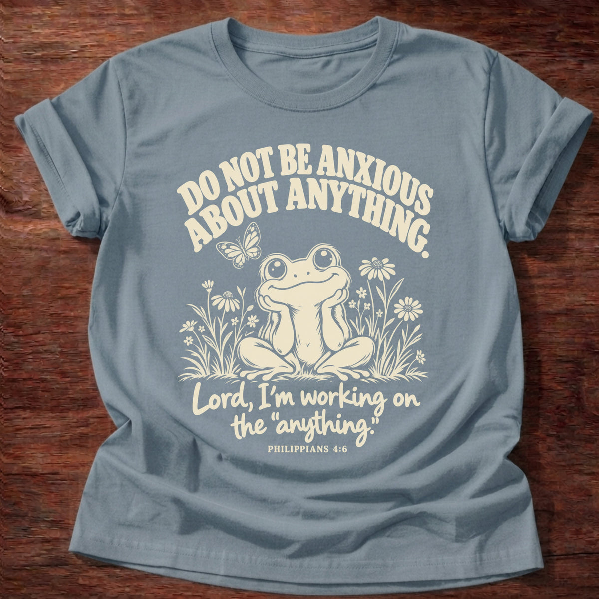 Anything Part T-Shirt in Stone Blue featuring a wide-eyed frog sitting among wildflowers and Philippians 4:6 anxiety humor design