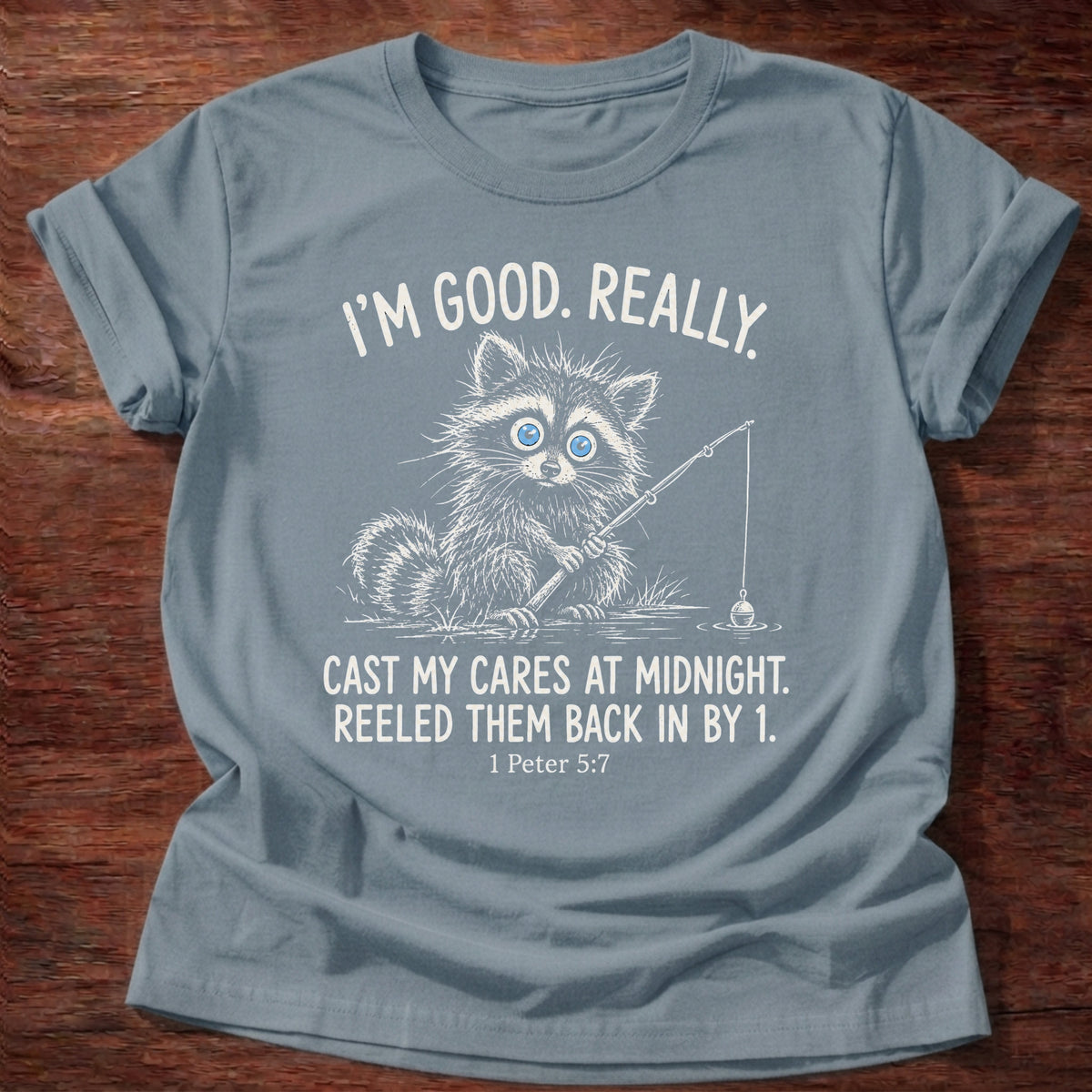 Stone Blue t-shirt printed with a raccoon holding a fishing rod graphic and “I'm good. Really. Cast my cares at midnight. Reeled them back in by 1.” 1 Peter 5:7 Christian shirt