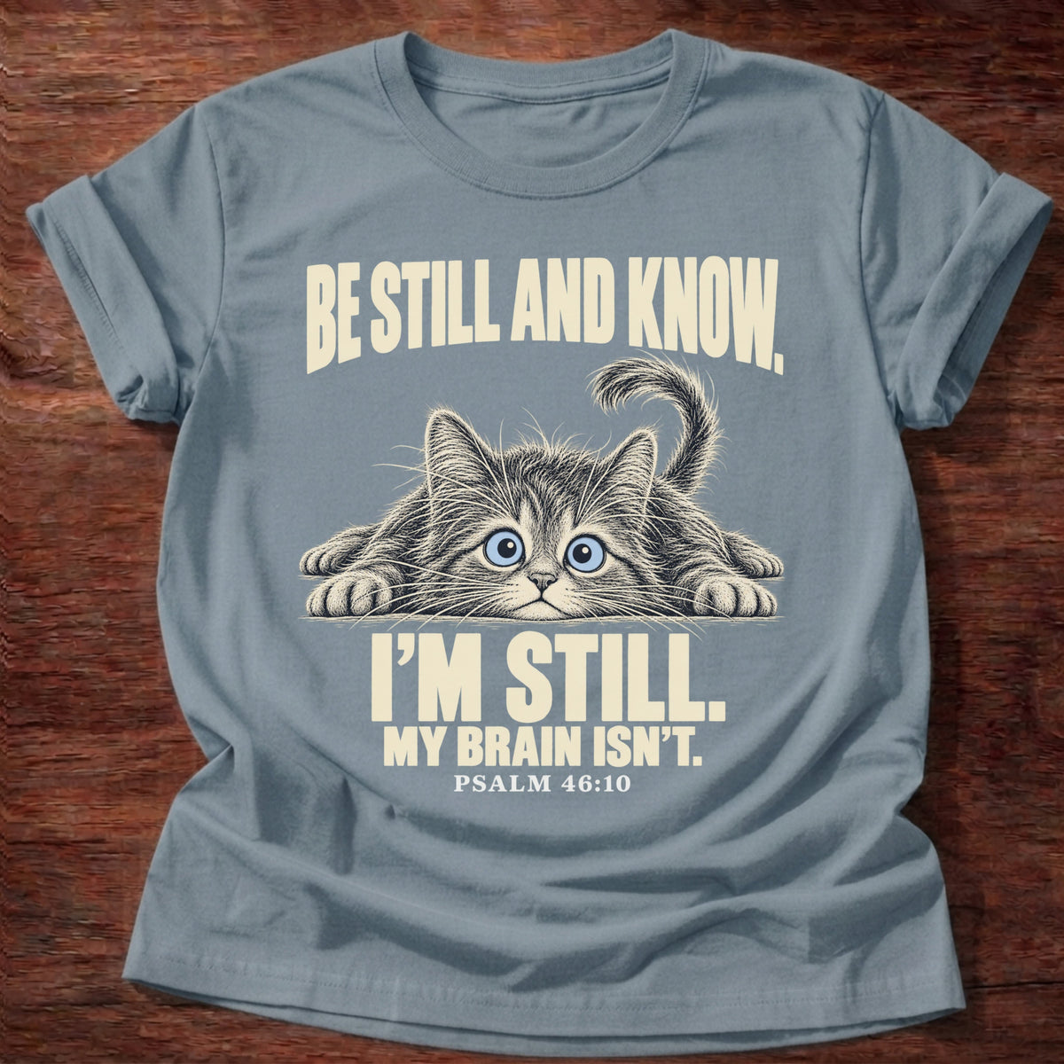 Brain Not Still T-Shirt in Stone Blue featuring a wide-eyed cat lying flat with alert eyes and Psalm 46:10 overthinking humor design
