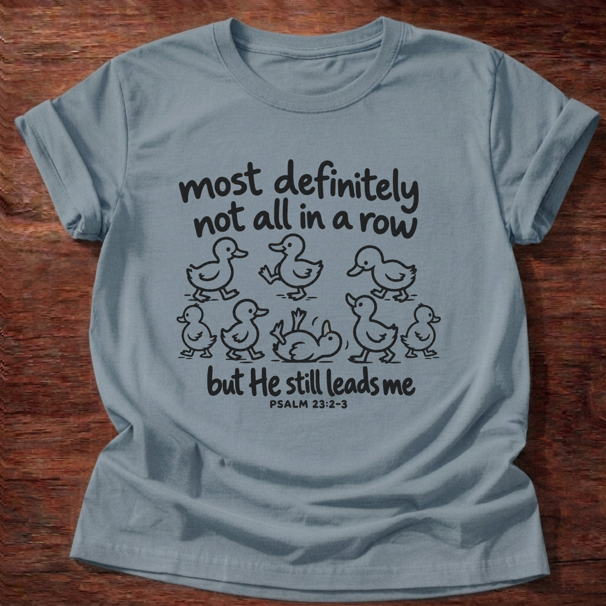 Stone Blue t-shirt printed with a scattered line of hand-drawn ducklings graphic and “Most definitely not all in a row, but He still leads me.” Psalm 23:2-3 Christian shirt