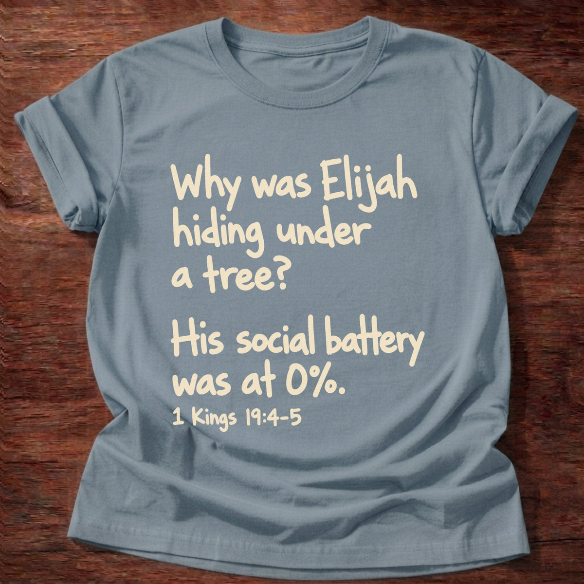 Stone Blue t-shirt printed with a simple hand-lettered Bible joke graphic and “Why was Elijah hiding under a tree? His social battery was at 0%.” 1 Kings 19:4-5 Christian shirt