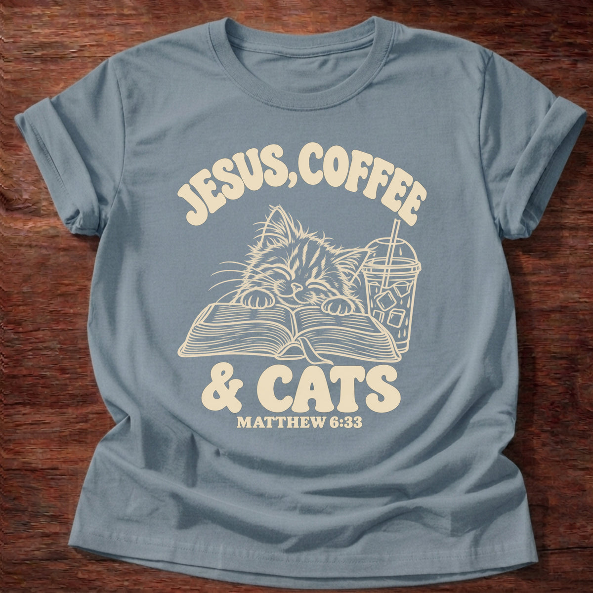 Stone Blue t-shirt printed with a kitten reading an open Bible beside an iced coffee and “Jesus, Coffee & Cats” Matthew 6:33 Christian shirt