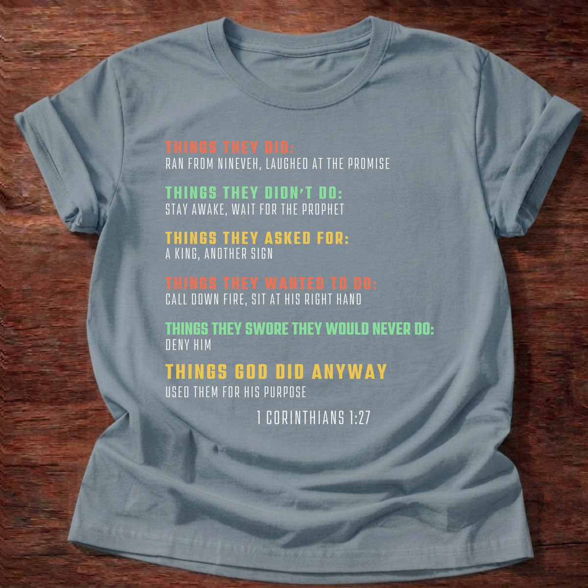 Stone Blue t-shirt printed with bold colorful typography listing what Bible heroes did graphic and “Things they did. Things God did anyway.” 1 Corinthians 1:27 Christian shirt