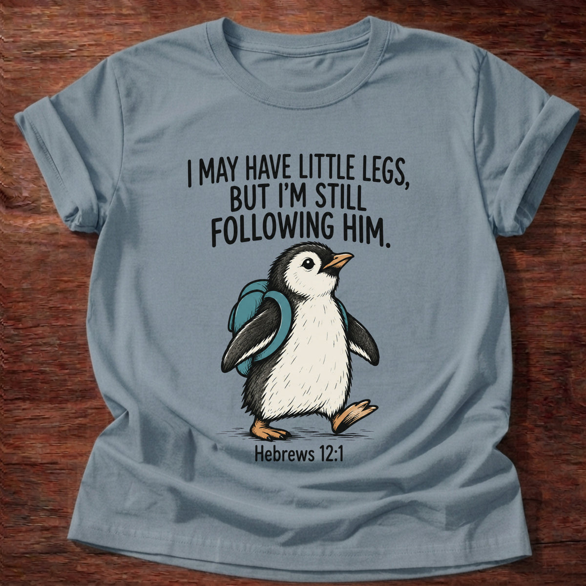 Stone Blue t-shirt printed with a penguin graphic and 'I may have little legs, but I'm still following Him.' Hebrews 12:1 faith based gift