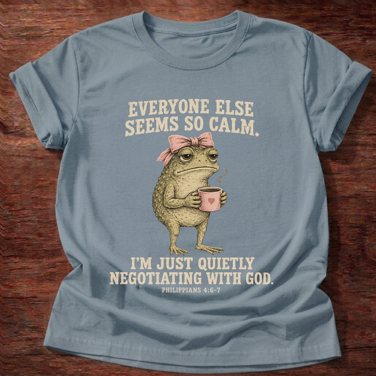 Stone Blue t-shirt printed with a possum holding a tea cup graphic and 'Everyone else seems so calm. I'm just quietly negotiating with God.' Philippians 4:6-7 faith based gift
