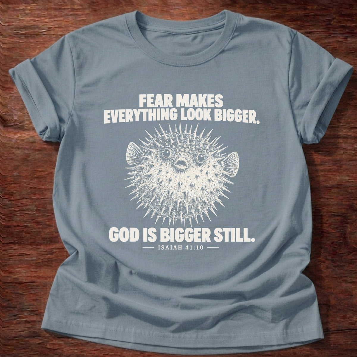 Stone Blue t-shirt printed with a pufferfish inflated to look bigger graphic and 'Fear makes everything look bigger. God is bigger still.' Isaiah 41:10 faith based gift