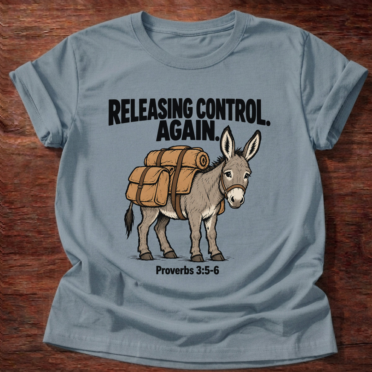 Stone Blue t-shirt printed with a donkey carrying a backpack graphic and 'Releasing control. Again.' Proverbs 3:5-6 faith based gift