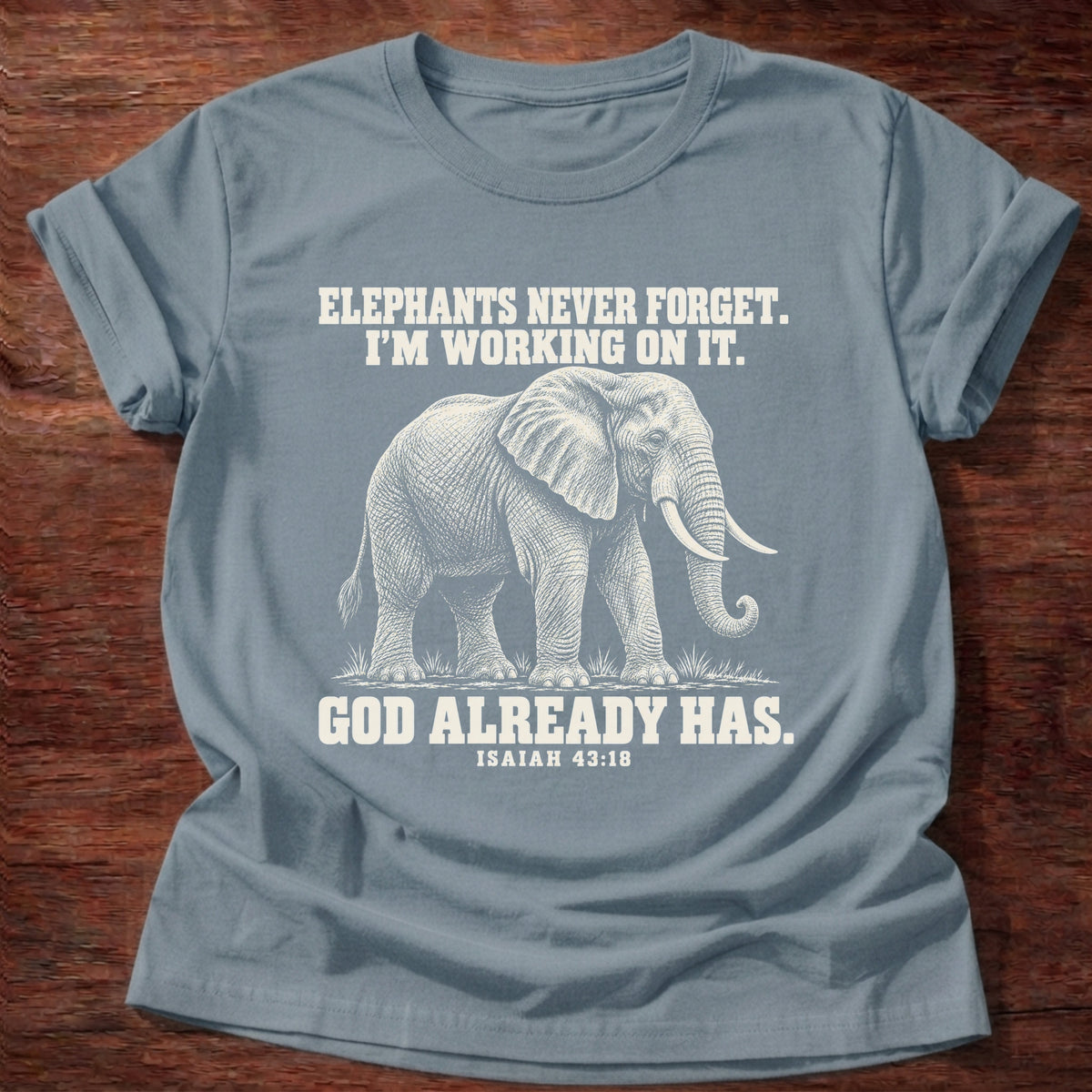 Stone Blue t-shirt printed with an elephant walking through tall grass graphic and 'Elephants never forget. I'm working on it. God already has.' Isaiah 43:18 faith based gift
