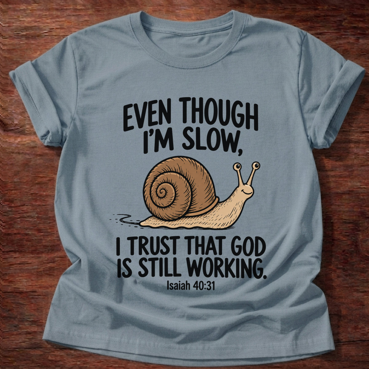 Stone Blue t-shirt printed with a snail graphic and 'Even though I'm slow. I trust that God is still working.' Isaiah 40:31 faith based gift