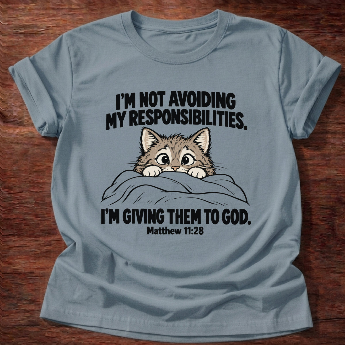 Stone Blue t-shirt printed with a cat peeking over a blanket graphic and 'I'm not avoiding my responsibilities. I'm giving them to God.' Matthew 11:28 faith based gift