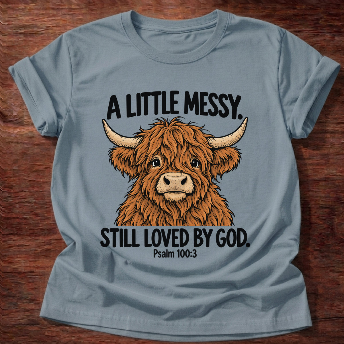 Stone Blue t-shirt printed with a highland cow graphic and 'A little messy. Still loved by God.' Psalm 100:3 faith based gift