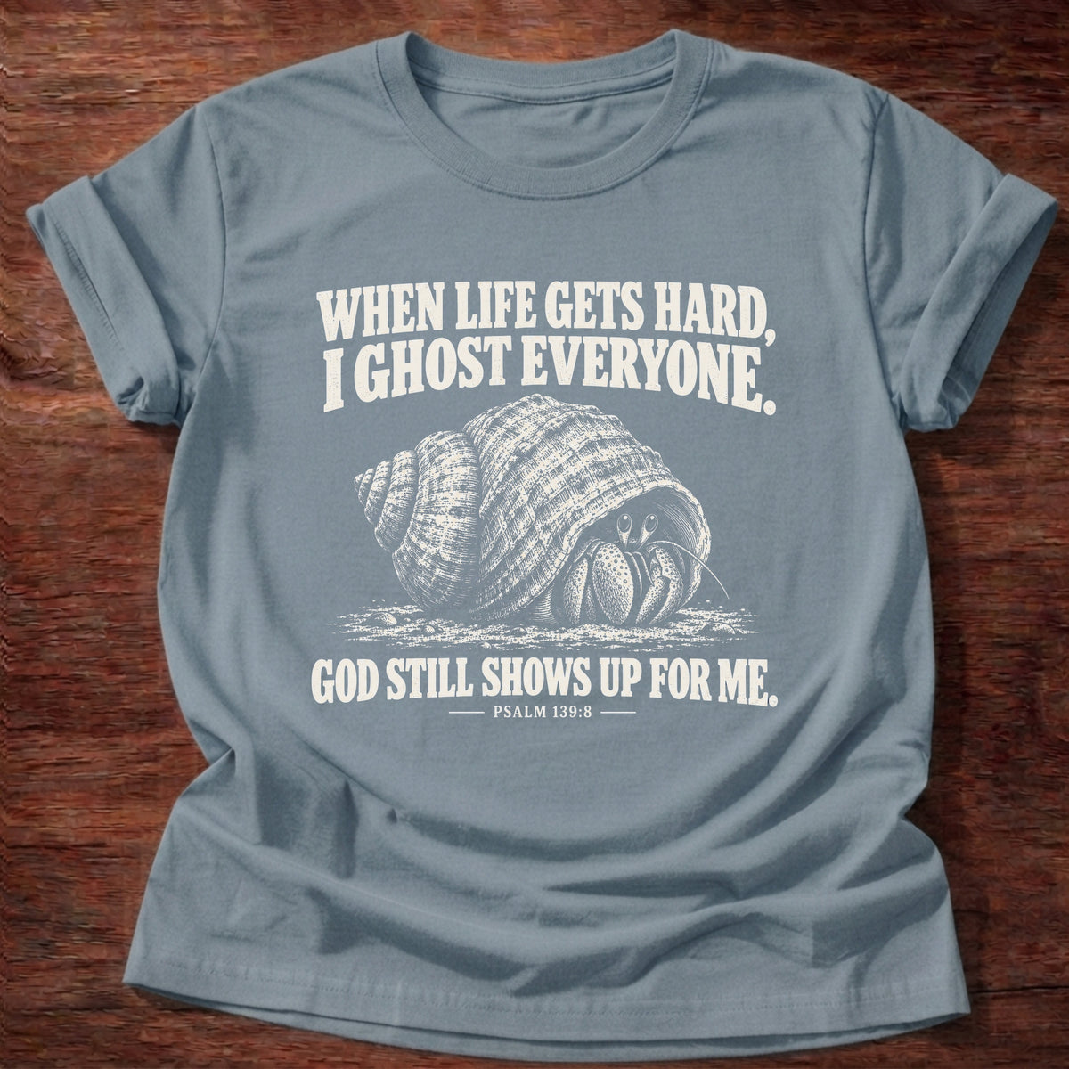 Stone Blue t-shirt printed with a hermit crab retreating into its shell graphic and 'When life gets hard, I ghost everyone. God still shows up for me.' Psalm 139:8 faith based gift
