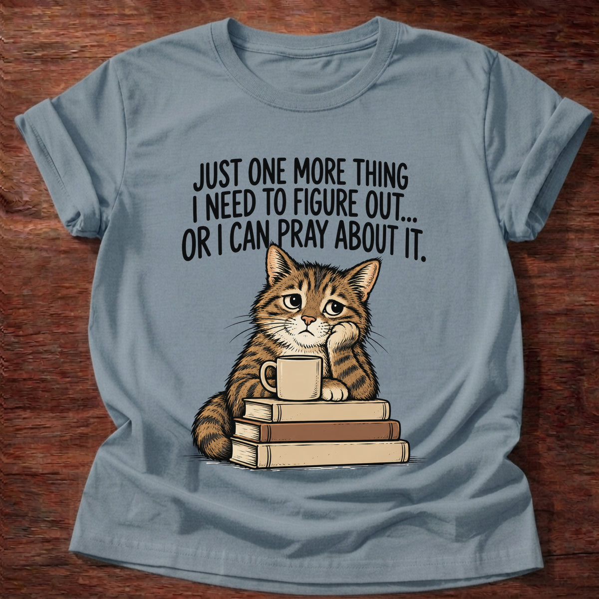 Stone Blue t-shirt printed with a cat surrounded by books graphic and 'Just one more thing I need to figure out... or I can pray about it.' Philippians 4:6-7 faith based gift