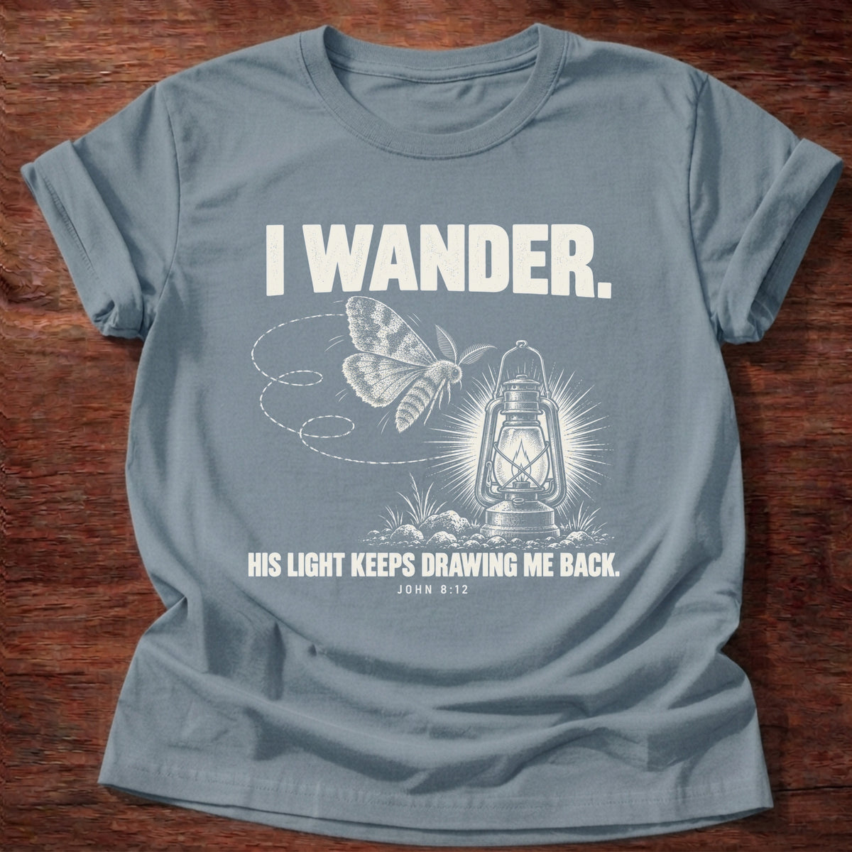 Stone Blue t-shirt printed with a moth circling a glowing lantern graphic and 'I wander. His light keeps drawing me back.' John 8:12 faith based gift