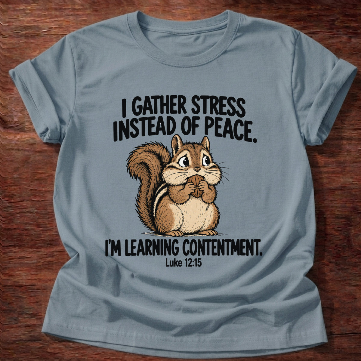 Stone Blue t-shirt printed with a squirrel gathering acorns graphic and 'I gather stress instead of peace. I'm learning contentment.' Luke 12:15 faith based gift