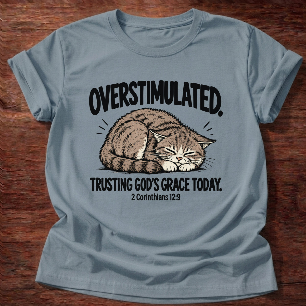 Stone Blue t-shirt printed with a cat curled asleep graphic and 'Overstimulated. Trusting God's grace today.' 2 Corinthians 12:9 faith based gift