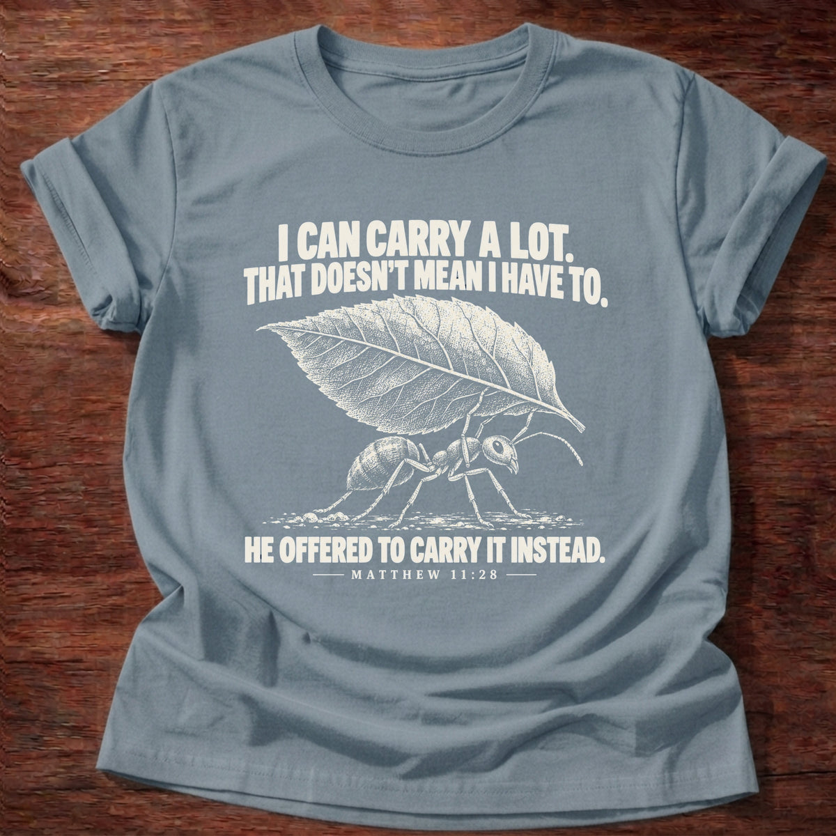 Stone Blue t-shirt printed with an ant hauling a leaf many times its size graphic and 'I can carry a lot. That doesn't mean I have to. He offered to carry it instead.' Matthew 11:28 faith based gift