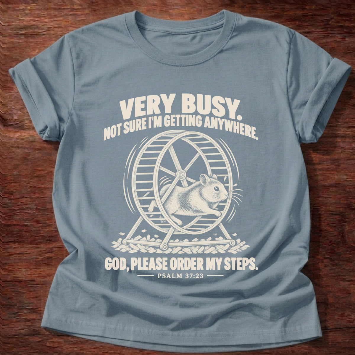 Stone Blue t-shirt printed with a squirrel running on a wheel graphic and 'Very busy. Not sure I'm getting anywhere. God, please order my steps.' Psalm 37:23 faith based gift
