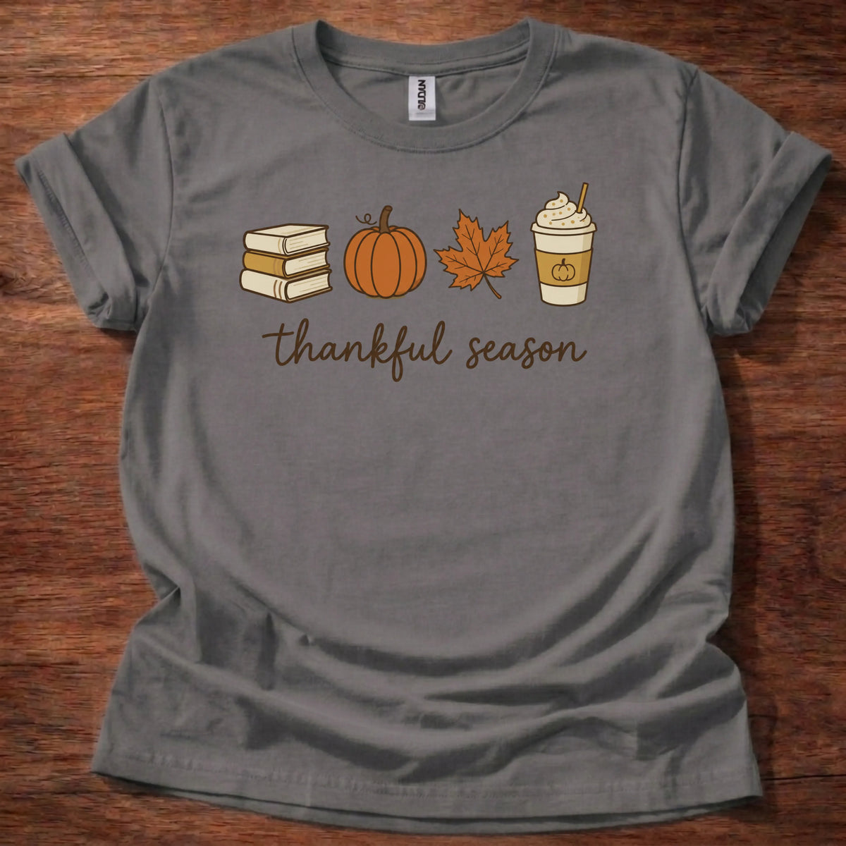 Charcoal t-shirt with a minimal icon row of books, a pumpkin, a maple leaf, and a coffee cup above soft script reading thankful season